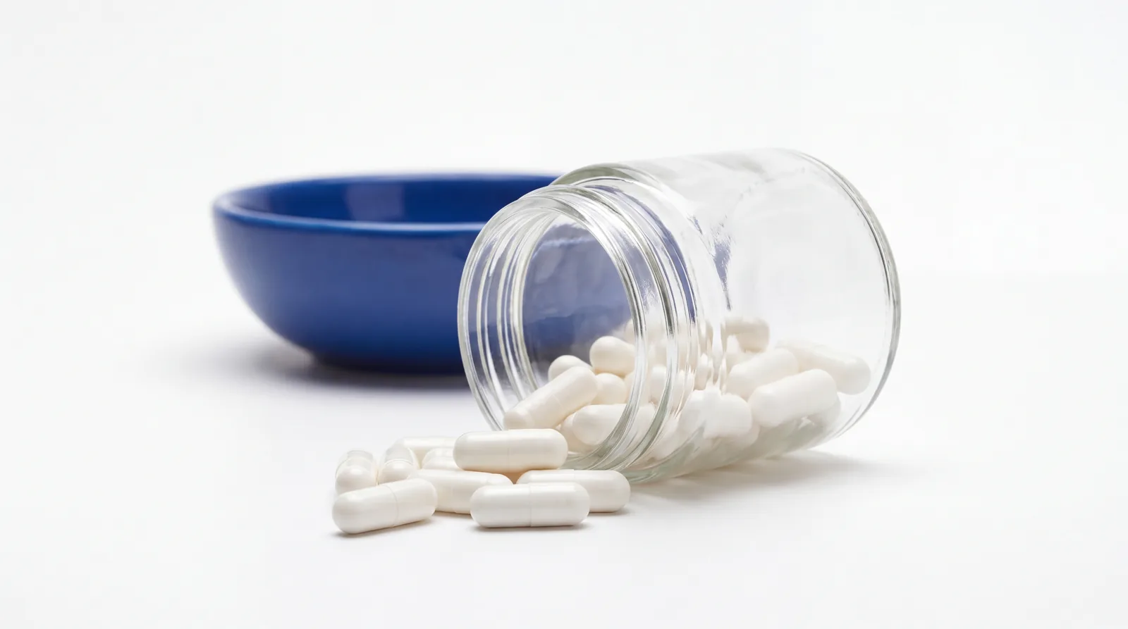 Plain white capsules spilling from an unlabelled glass jar