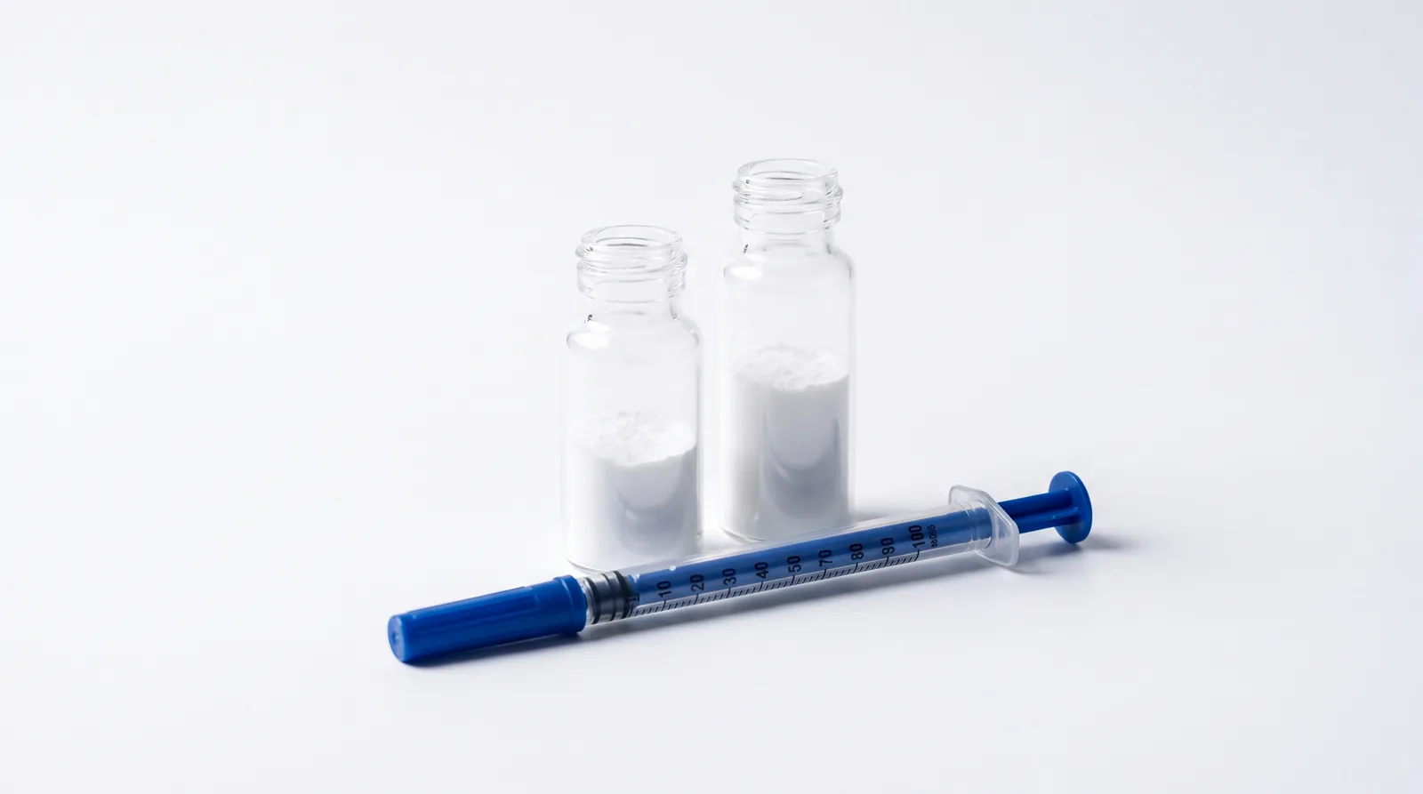 Two unlabelled vials of different heights with an insulin syringe in front