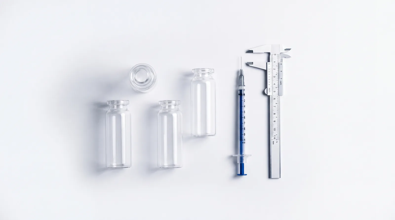 Overhead flat lay of four unlabelled vials with a syringe and calipers