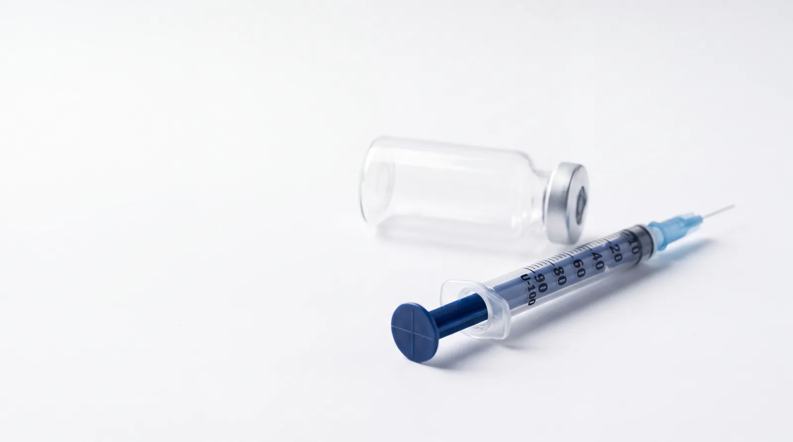 Insulin syringe in sharp focus with a vial resting behind it