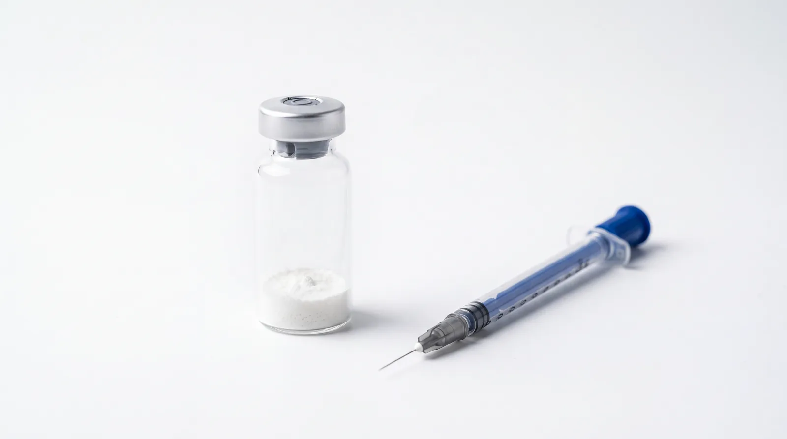Unlabelled vial of lyophilised powder standing beside a U-100 insulin syringe